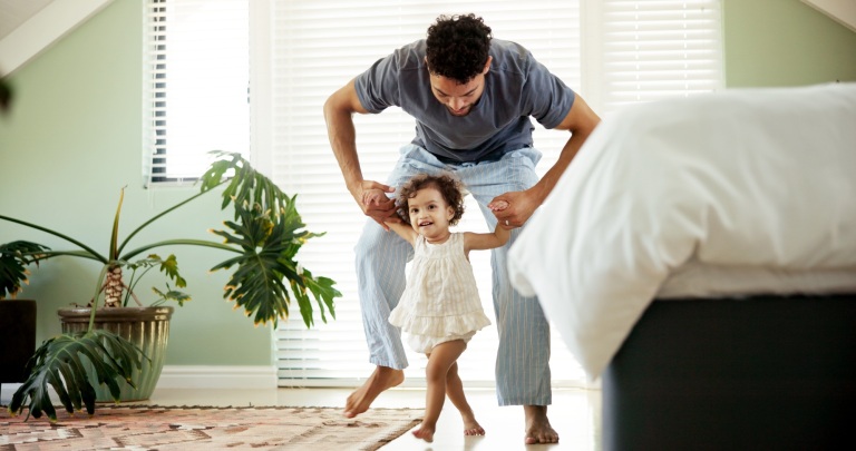 Dad, child and learning to walk in home with holding hands, first steps and support with milestone.